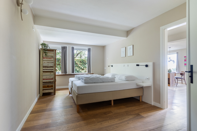 Lichte slaapkamer met openslaande deuren en houten vloer in vakantiehuis Boszicht 16a Schiermonnikoog